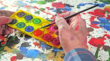 Bir sanatçı fırçaya suluboya boya uygular. Ellerine yakın çekim..