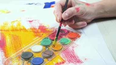 Bir sanatçı fırçaya suluboya boya uygular. Ellerine yakın çekim..