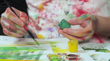 Beyaz önlüklü bir sanatçı resim fırçasını bir kap dolusu gustara batırıyor..