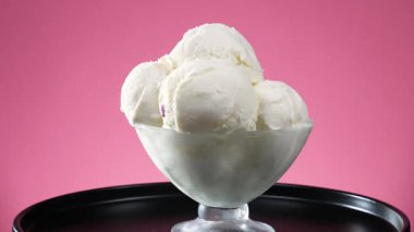 Bardakta vanilyalı dondurma, parlak bir arka planda yavaşça dönüyor..