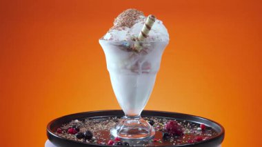 Cam bir kasede meyveli dondurma, yenilebilir konfeti serpilmiş, parlak bir arka planda yavaşça dönüyor..