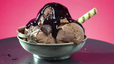 Çikolata jölesiyle ıslatılmış metal bir kasede meyveli dondurma. Parlak bir arka planda yavaşça dönüyor..