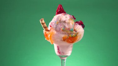 Yenilebilir konfeti serpilmiş cam bir kasede meyveli dondurma yavaşça parlak bir arka planda döner..