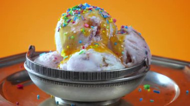 Yenilebilir konfeti serpiştirilmiş metal bir kasedeki vanilyalı dondurma yavaşça parlak bir arka plana doğru dönüyor..