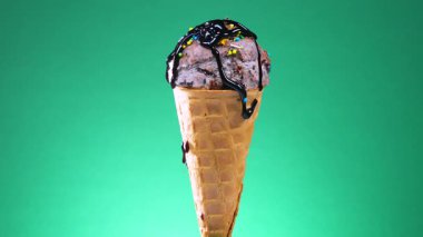 Parlak renkli arka planda waffle külahında çikolatalı dondurma, kendi ekseni etrafında yavaşça dönüyor..