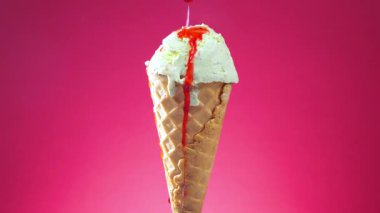Pistachio dondurması parlak renkli arka planda waffle külahında yavaşça ekseni etrafında döner ve kırmızı meyve şurubuyla ıslanır..