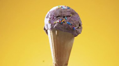 Parlak renkli arka planda waffle külahında dondurma, kendi ekseni etrafında yavaşça döner, erir ve aşağı damlar.