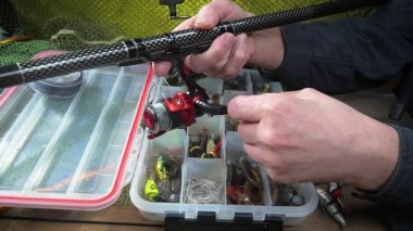 Bir balıkçı balık tutmadan önce takımlarını toplayıp kontrol eder. Ellerine yakın çekim..