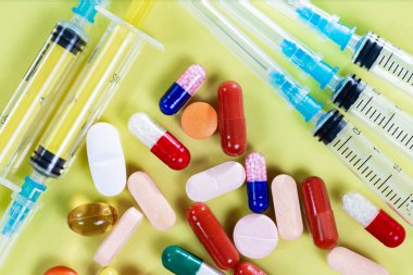 Tabletler, bir termometre ve sarı zemin üzerinde şırıngalar. Yukarıdan görüntüle.