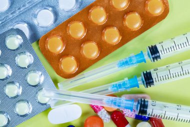 Tabletler, bir termometre ve sarı zemin üzerinde şırıngalar. Yukarıdan görüntüle.