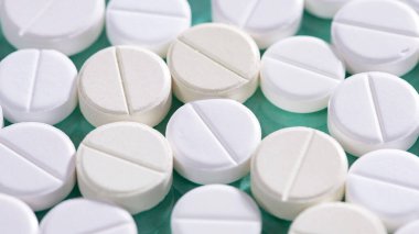 Masaya saçılmış beyaz yuvarlak tabletler, yeşil bir zemin üzerine.