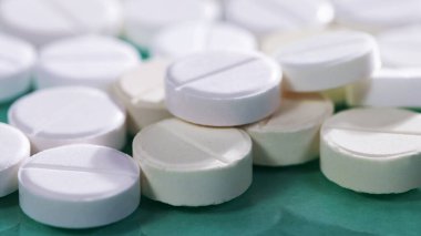 Masaya saçılmış beyaz yuvarlak tabletler, yeşil bir zemin üzerine.