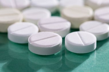 Masaya saçılmış beyaz yuvarlak tabletler, yeşil bir zemin üzerine.