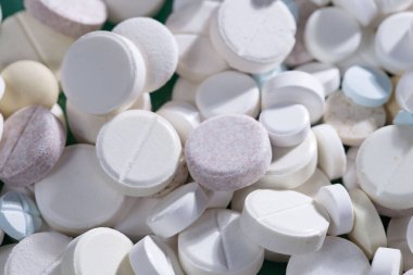 Masaya saçılmış beyaz yuvarlak tabletler, yeşil bir zemin üzerine.