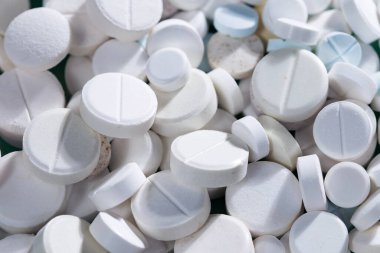 Masaya saçılmış beyaz yuvarlak tabletler, yeşil bir zemin üzerine.