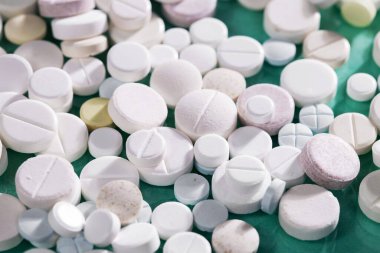 Masaya saçılmış beyaz yuvarlak tabletler, yeşil bir zemin üzerine.