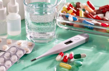 Bir bardak su, bir termometre ve renkli bir arka plan üzerine haplar. Yakın plan..