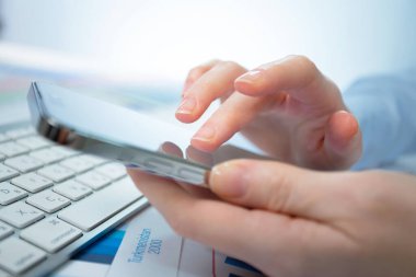 Ofiste bir kadın akıllı telefonuyla çalışıyor, bir rapor üzerinde. Ellerine yakın çekim..