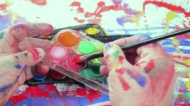 Sanatçının elleri, sanatta yaratıcı imgeler yaratmak için çalışır. Resim boyaları ve fırçalar, palet, guaj ve suluboya kullanarak tuvale çok renkli dokunuşlar uyguluyorlar..