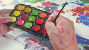 Sanatçının elleri, sanatta yaratıcı imgeler yaratmak için çalışır. Resim boyaları ve fırçalar, palet, guaj ve suluboya kullanarak tuvale çok renkli dokunuşlar uyguluyorlar..