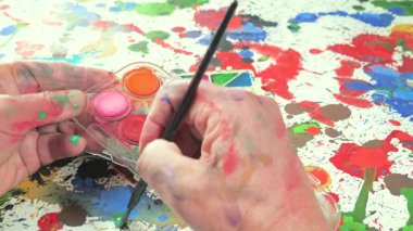 Sanatçının elleri, sanatta yaratıcı imgeler yaratmak için çalışır. Resim boyaları ve fırçalar, palet, guaj ve suluboya kullanarak tuvale çok renkli dokunuşlar uyguluyorlar..