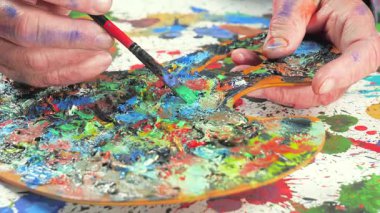 Sanatçının elleri, sanatta yaratıcı imgeler yaratmak için çalışır. Resim boyaları ve fırçalar, palet, guaj ve suluboya kullanarak tuvale çok renkli dokunuşlar uyguluyorlar..