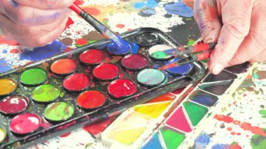 Sanatçının elleri, sanatta yaratıcı imgeler yaratmak için çalışır. Resim boyaları ve fırçalar, palet, guaj ve suluboya kullanarak tuvale çok renkli dokunuşlar uyguluyorlar..