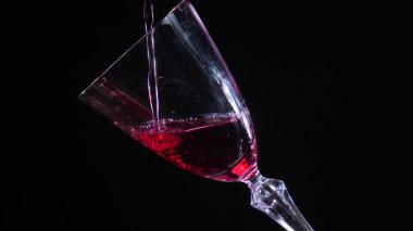 Kırmızı kuru şarap, şişeden bardağa dökülüyor, siyah arka planda. Yakın plan. Yavaş çekim.