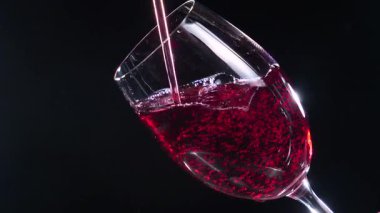 Kırmızı kuru şarap, şişeden bardağa dökülüyor, siyah arka planda. Yakın plan. Yavaş çekim.
