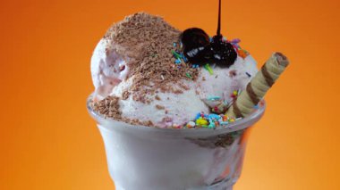 Çikolatalı şekerle serpiştirilmiş cam vazoda vanilyalı dondurma, yavaşça kendi ekseni etrafında dönüyor..