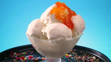 Meyve şurubuyla ıslatılmış cam bir kasede vanilyalı dondurma, yavaş yavaş parlak bir arka plana doğru dönüyor ve eriyor.