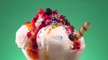 Yenilebilir konfeti serpilmiş cam bir kasede meyveli dondurma yavaşça parlak bir arka planda döner..