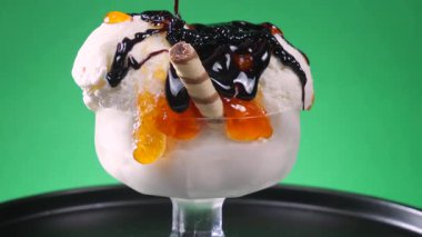Çikolatalı şekerle serpiştirilmiş cam bir kasede vanilyalı dondurma, yavaş yavaş parlak bir arkaplanda dönüyor ve eriyor.