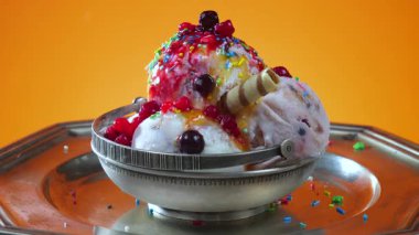 Yenilebilir konfeti serpiştirilmiş metal kasede vanilyalı dondurma, parlak bir arka planda yavaşça dönüyor..