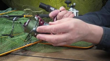 Stüdyo kompozisyonunda bir masada spor balıkçılık ekipmanları, bir ağın arka planına karşı. Balıkçının elleri, olta takımını kontrol eder..