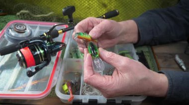 Stüdyo kompozisyonunda bir masada spor balıkçılık ekipmanları, bir ağın arka planına karşı. Balıkçının elleri, olta takımını kontrol eder..