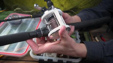 Stüdyo kompozisyonunda bir masada spor balıkçılık ekipmanları, bir ağın arka planına karşı. Balıkçının elleri, olta takımını kontrol eder..