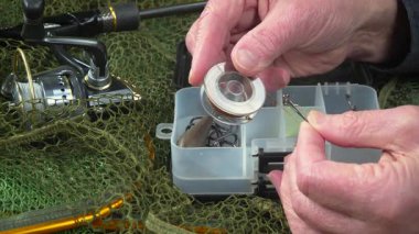 Stüdyo kompozisyonunda bir masada spor balıkçılık ekipmanları, bir ağın arka planına karşı. Balıkçının elleri, olta takımını kontrol eder..