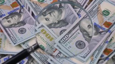 Yaşlı bir muhasebecinin elleri 100 dolarlık banknotları ayırıyor ve büyüteçle inceliyor..