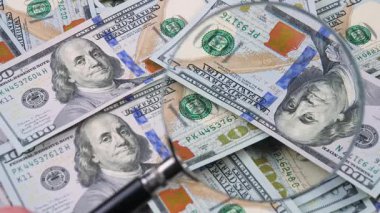 Yaşlı bir muhasebecinin elleri 100 dolarlık banknotları ayırıyor ve büyüteçle inceliyor..