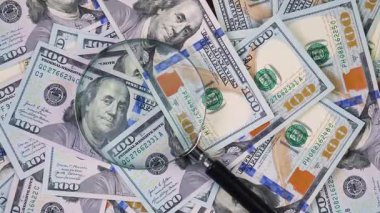 Bir büyüteç kaotik bir şekilde düzenlenmiş 100 dolarlık banknotların üzerine yavaşça iner. Yukarıdan görüntüle.