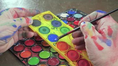 Sanatçının elleri, sanatta yaratıcı imgeler yaratmak için çalışır. Resim boyaları ve fırçalar, palet, guaj ve suluboya kullanarak tuvale çok renkli dokunuşlar uyguluyorlar..