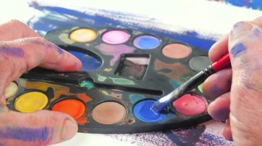 Sanatçının elleri, sanatta yaratıcı imgeler yaratmak için çalışır. Resim boyaları ve fırçalar, palet, guaj ve suluboya kullanarak tuvale çok renkli dokunuşlar uyguluyorlar..