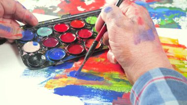 Sanatçının elleri, sanatta yaratıcı imgeler yaratmak için çalışır. Resim boyaları ve fırçalar, palet, guaj ve suluboya kullanarak tuvale çok renkli dokunuşlar uyguluyorlar..