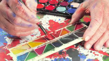 Sanatçının elleri, sanatta yaratıcı imgeler yaratmak için çalışır. Resim boyaları ve fırçalar, palet, guaj ve suluboya kullanarak tuvale çok renkli dokunuşlar uyguluyorlar..