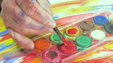 Sanatçının elleri, sanatta yaratıcı imgeler yaratmak için çalışır. Resim boyaları ve fırçalar, palet, guaj ve suluboya kullanarak tuvale çok renkli dokunuşlar uyguluyorlar..