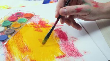 Sanatçının elleri, sanatta yaratıcı imgeler yaratmak için çalışır. Resim boyaları ve fırçalar, palet, guaj ve suluboya kullanarak tuvale çok renkli dokunuşlar uyguluyorlar..