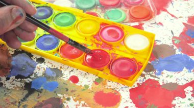 Sanatçının elleri, sanatta yaratıcı imgeler yaratmak için çalışır. Resim boyaları ve fırçalar, palet, guaj ve suluboya kullanarak tuvale çok renkli dokunuşlar uyguluyorlar..