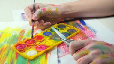 Sanatçının elleri, sanatta yaratıcı imgeler yaratmak için çalışır. Resim boyaları ve fırçalar, palet, guaj ve suluboya kullanarak tuvale çok renkli dokunuşlar uyguluyorlar..