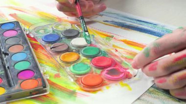 Sanatçının elleri, sanatta yaratıcı imgeler yaratmak için çalışır. Resim boyaları ve fırçalar, palet, guaj ve suluboya kullanarak tuvale çok renkli dokunuşlar uyguluyorlar..